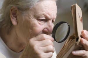 femme âgée atteinte de DMLA lisant avec une loupe 